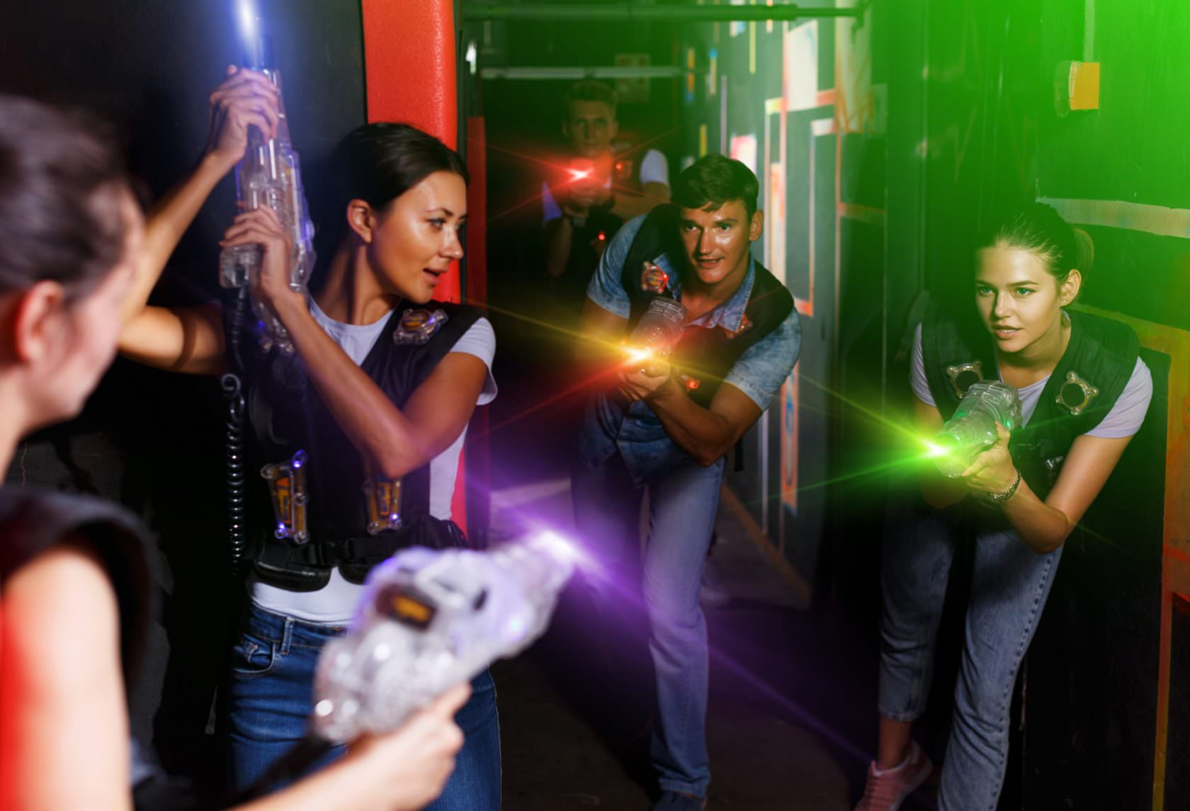 Portrait of active young friends standing with laser guns during laser tag game in dark room